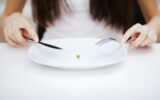 Eating disorder. Girl is holding a plate and trying to put a pea on the fork