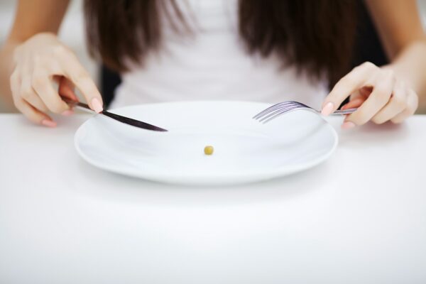 Eating disorder. Girl is holding a plate and trying to put a pea on the fork
