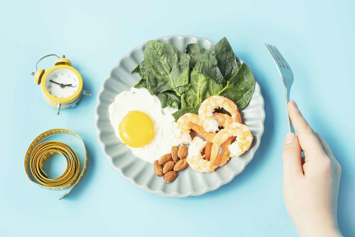 Female hand holds a fork next to a plate of food and centimeter tape, concept of a keto diet.