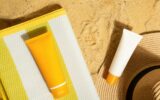 Orange and white tubes of sunscreen on beach next to straw hat and mat. Sun protection on vacation.