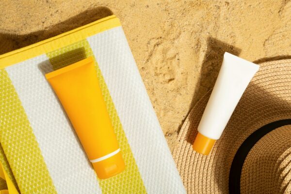 Orange and white tubes of sunscreen on beach next to straw hat and mat. Sun protection on vacation.