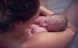 Over shoulder portrait of young woman holding new born baby daughter in birthing pool at home