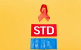 red ribbon as hiv awareness near std lettering and condoms isolated on orange