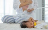 White shirt mother use breast milk pump to get breast milk and sitting near the sleeping newborn