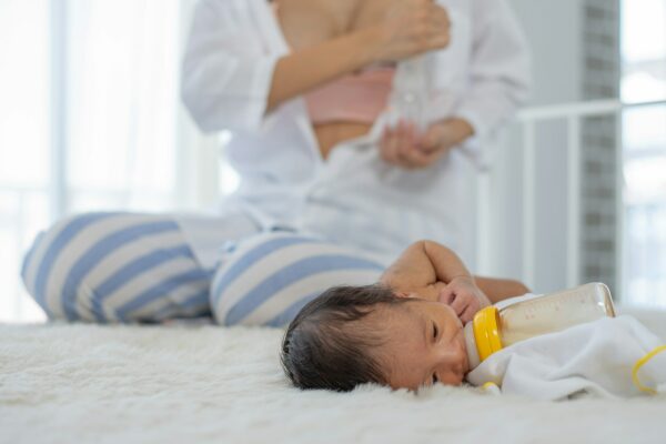 White shirt mother use breast milk pump to get breast milk and sitting near the sleeping newborn