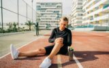 Young sport woman holding knee with hands in pain after suffering injury running. Runner woman sit
