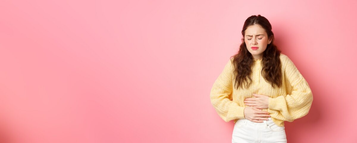 Young woman with pain in stomach, holding hands on belly, feeling terrible ache, menstrual cramps