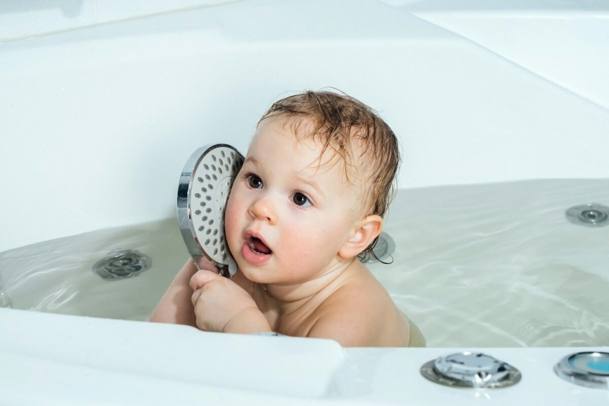 A little girl bathes in the bath and plays with a watering can.