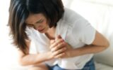 Asian woman having heart attack sitting on sofa.