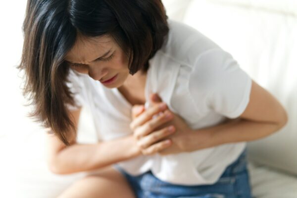 Asian woman having heart attack sitting on sofa.