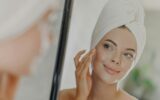 Beautiful woman touches face gently, looks at her reflection in mirror, enjoys softness of skin
