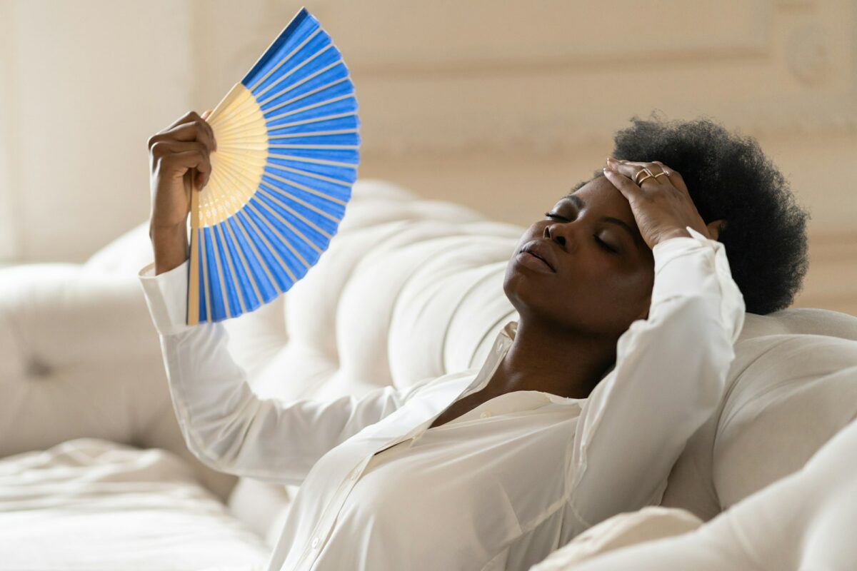 Black business woman suffering from heat stroke sitting in living room at home using waving fan