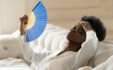 Black business woman suffering from heat stroke sitting in living room at home using waving fan