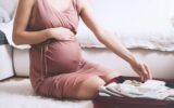 Close-up belly of pregnant woman with travel bag of clothes and necessities.