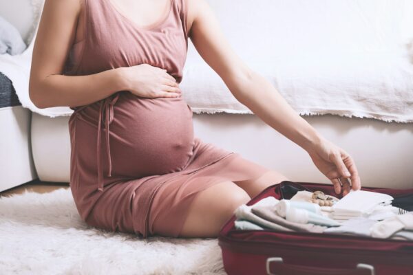 Close-up belly of pregnant woman with travel bag of clothes and necessities.