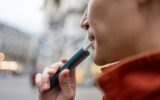Close up of a man vaping with electronic cigarette outdoor on street.