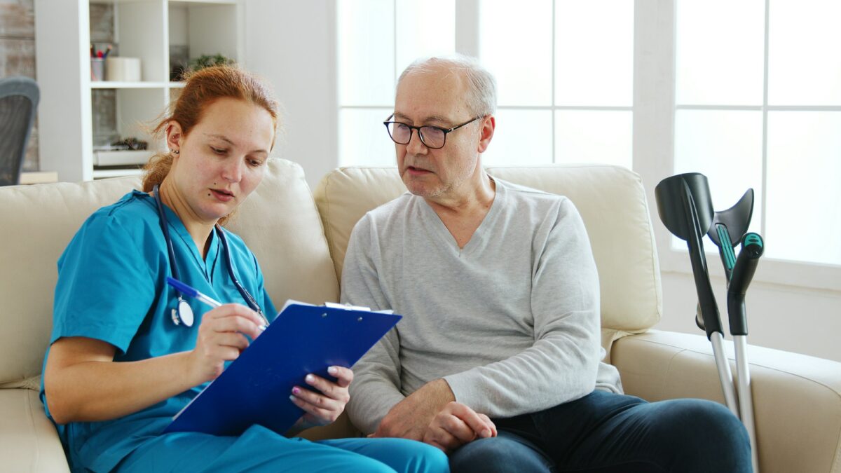 Female healthcare assistant taking notes about an old man health in cozy nursing home