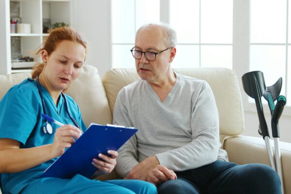 Female healthcare assistant taking notes about an old man health in cozy nursing home