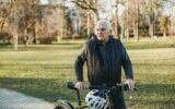 Man Walking a Bike Down a Sidewalk In City Park