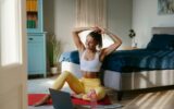Happy sporty woman adjusting hair and looking at laptop while preparing to home workout