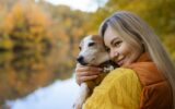 Portrait of a smiling young woman kissing a dog in a field. Dog lover stylish girl hugging her dog