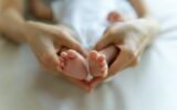 Tiny Newborn Baby's feet on female heart Shaped hands seen in top view.