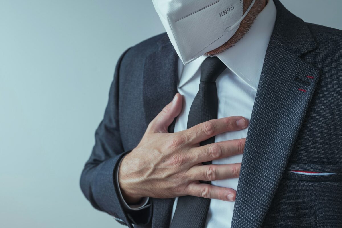 Elegant businessman with protective respiratory KN95 mask having severe aching chest pain symptoms