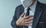 Elegant businessman with protective respiratory KN95 mask having severe aching chest pain symptoms