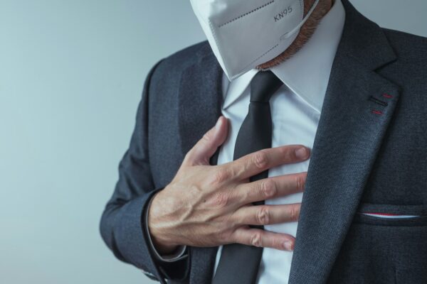 Elegant businessman with protective respiratory KN95 mask having severe aching chest pain symptoms
