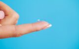 Young woman holding contact lens on finger.