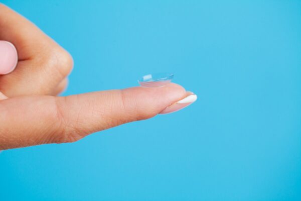 Young woman holding contact lens on finger.