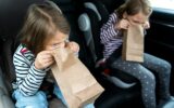 Little girls, sisters are driving in car. Children are sick, vomit into paper bag. Traveling on road