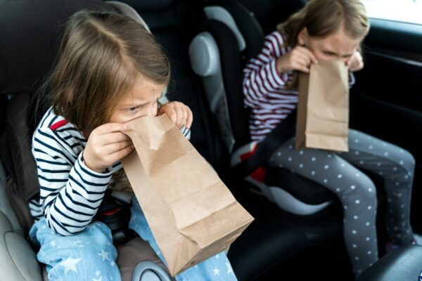 Little girls, sisters are driving in car. Children are sick, vomit into paper bag. Traveling on road
