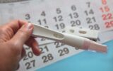 Person holding a positive Pregnancy test on calendar background