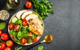 Green salad with grilled chicken meat at black table.