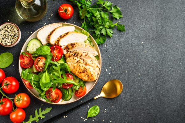 Green salad with grilled chicken meat at black table.