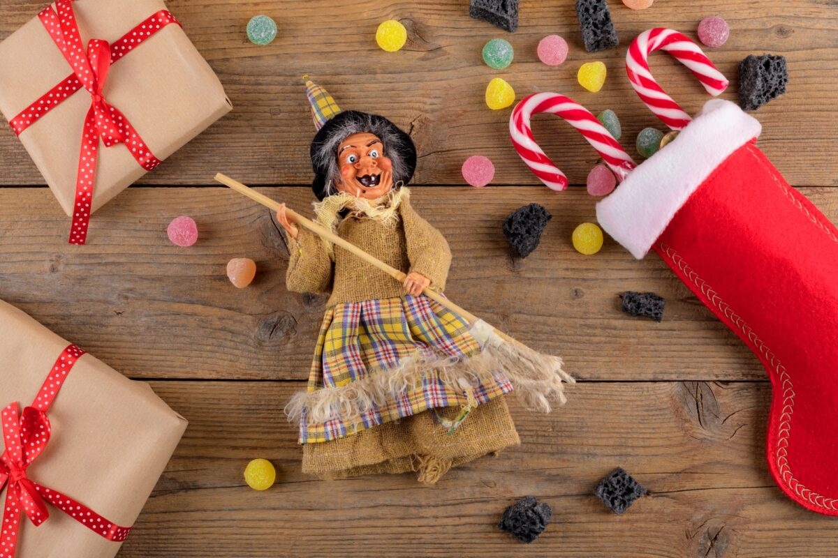 The witch Befana and red stocking with sweet coal and candy on rustic wooden background